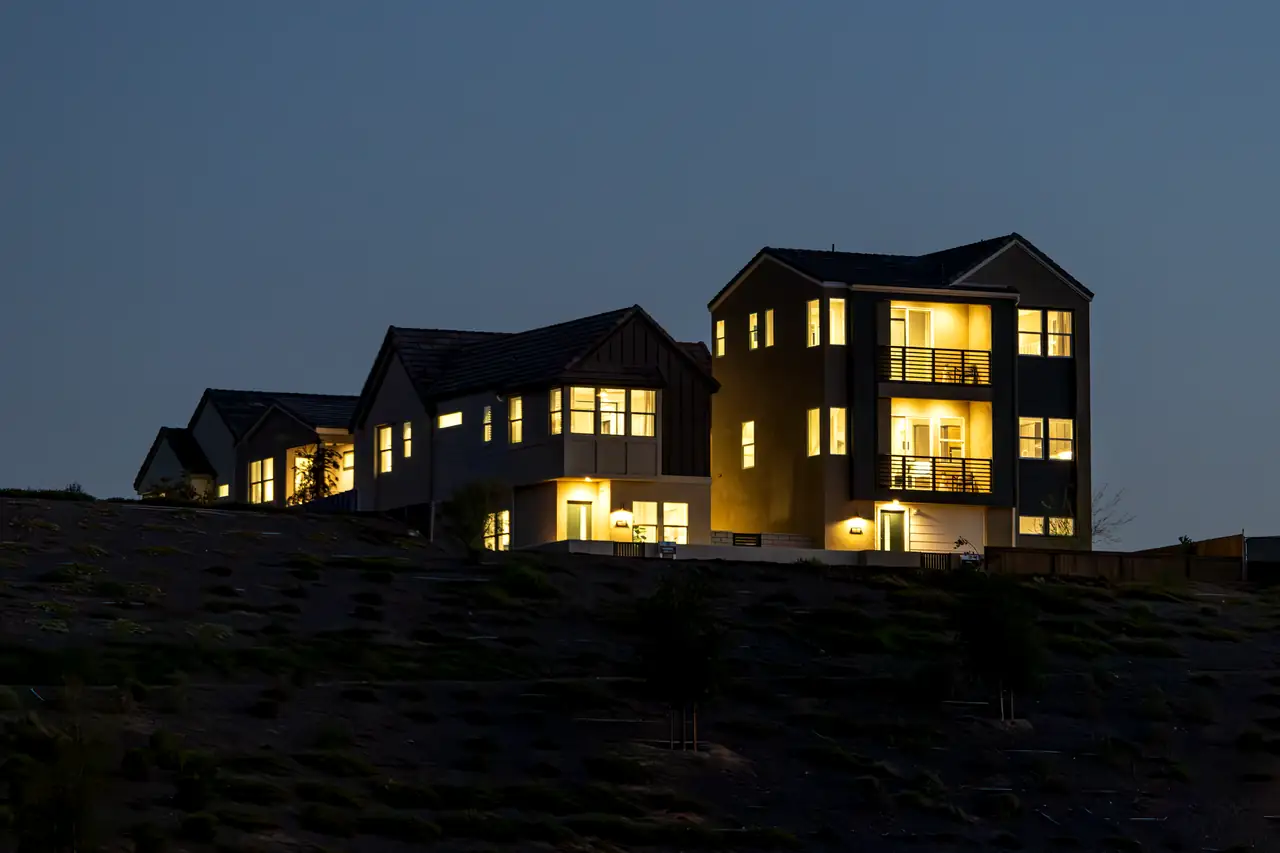 Brightly lit modern house on a hill at dusk, showcasing urban residential architecture.