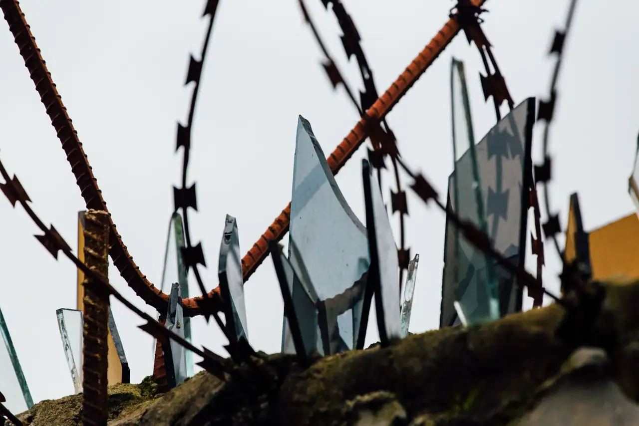 Close-up view of rusted barbed wire with jagged broken glass, conveying danger and security.